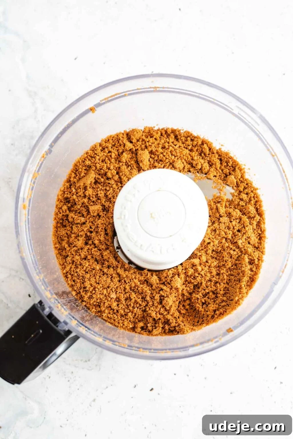 4-Ingredient No-Bake Biscoff Truffles 5 Finely crushed Biscoff cookie crumbs in a food processor, ready for the next step, on a light marble background.