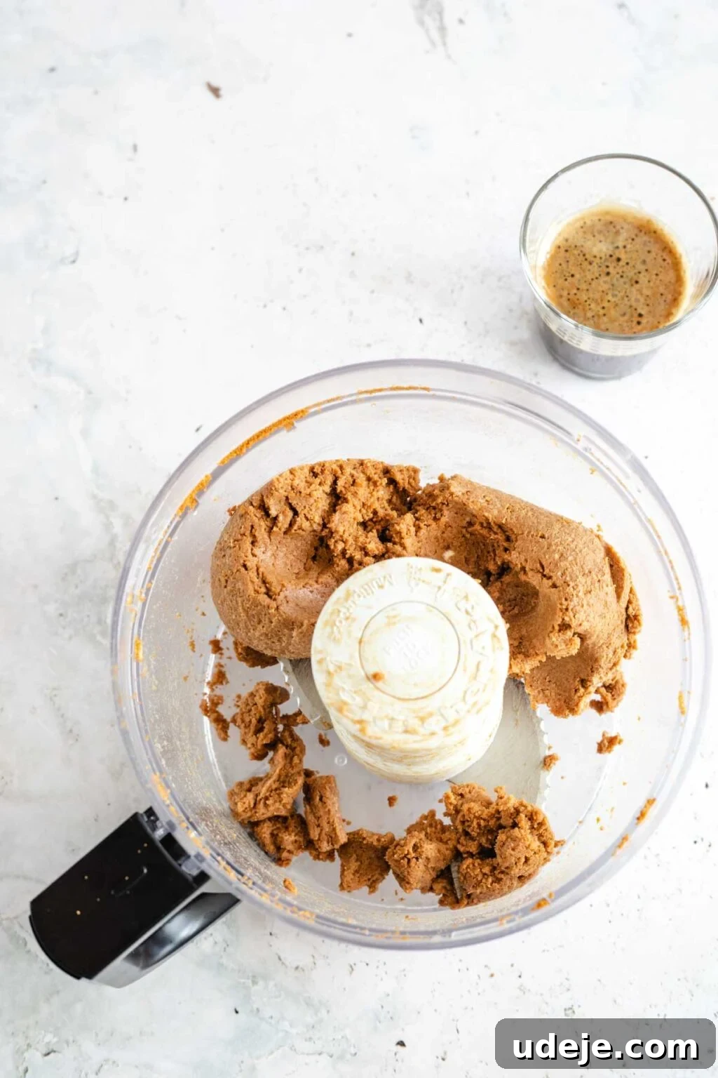 4-Ingredient No-Bake Biscoff Truffles 8 Biscoff truffle dough inside a food processor, accompanied by a freshly brewed shot of espresso on a light marbled background, ready to be incorporated.
