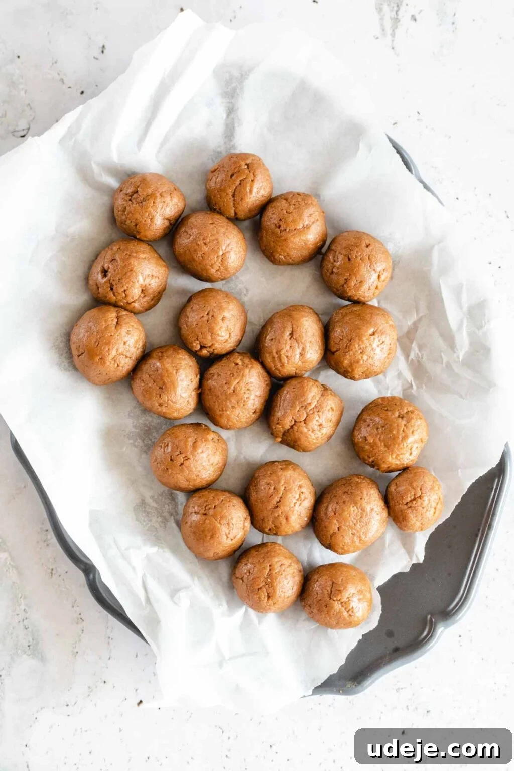 4-Ingredient No-Bake Biscoff Truffles 10 Neatly arranged Biscoff truffle balls on parchment paper, laid out on a gray tray, all on a light marbled background, chilling before coating.