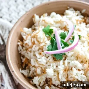 Cooked Egyptian rice and vermicelli in a beige bowl with slices of red onion and cilantro on top on a woven background and a fork beside the bowl of rice