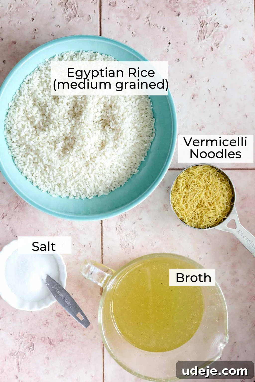 Egyptian Cloud Rice 5 Ingredient shot for Egyptian rice with rice in a blue bowl, vermicelli in a metal measuring cup, broth in a measuring cup and salt in a bowl with a spoon on a pink tiled background