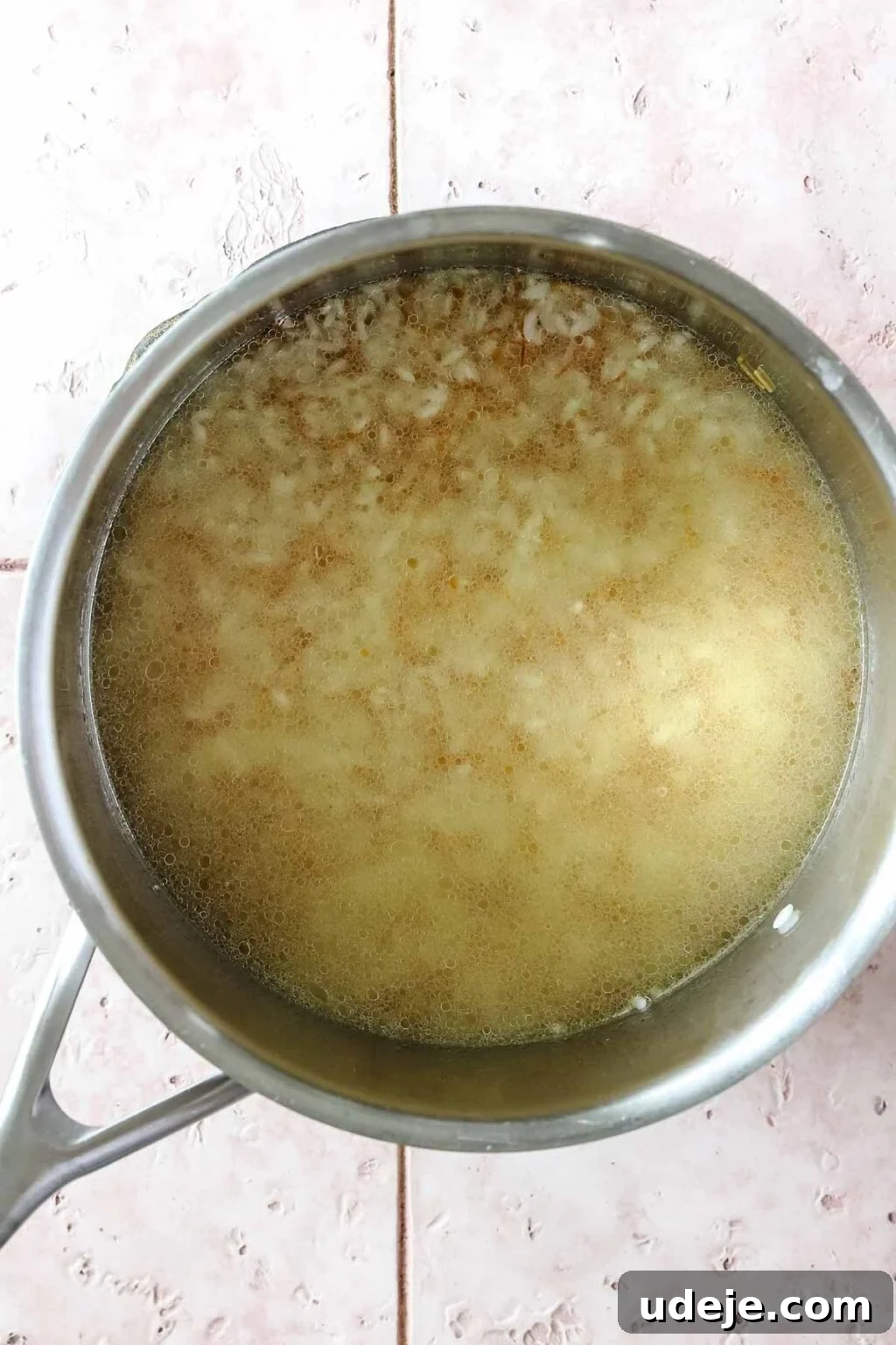 Egyptian Cloud Rice 9 Vermicelli and Egyptian rice in a metal saucepan covered in broth on a pink tiled background