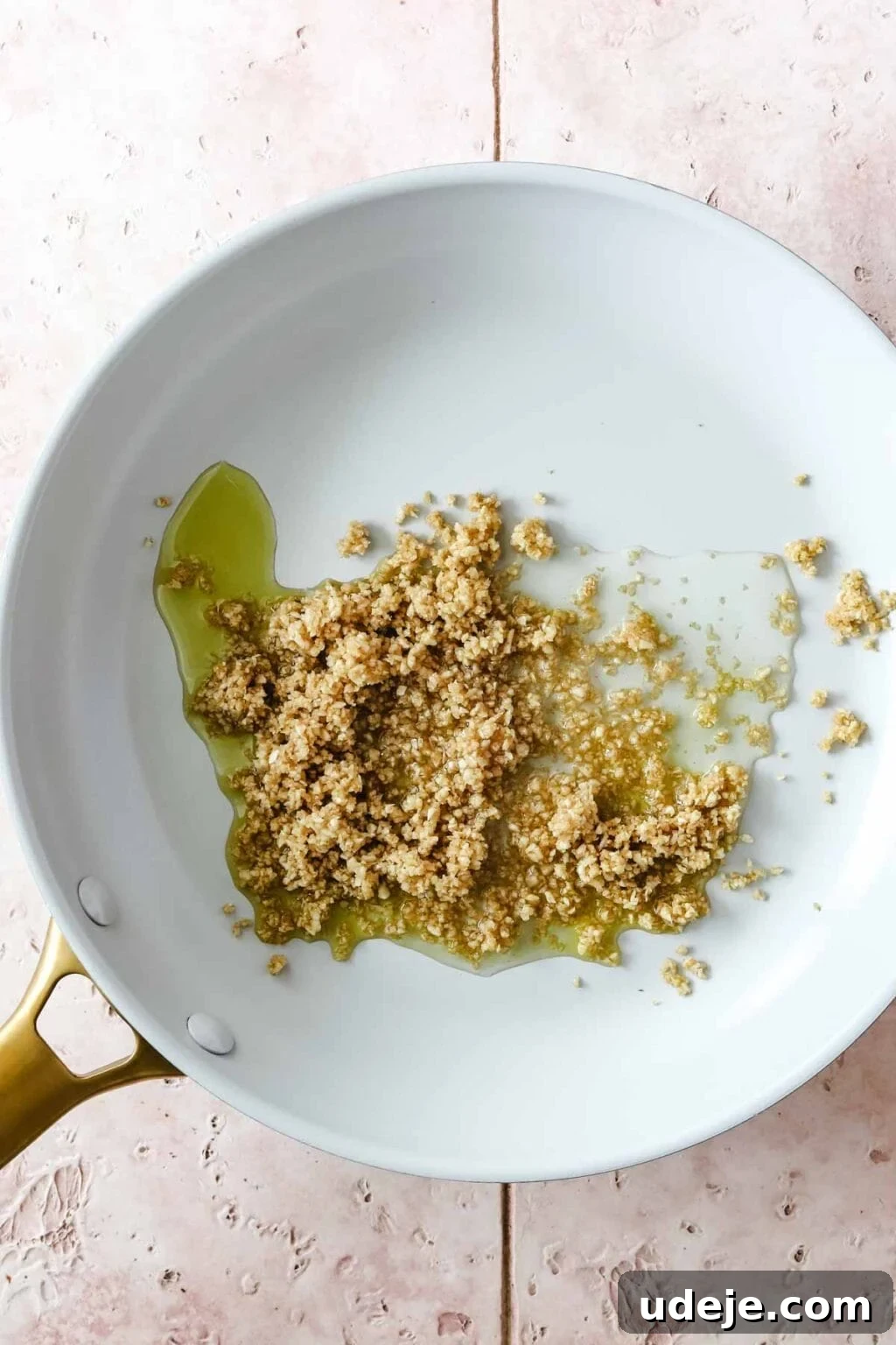 Molokhia: A Timeless Tradition 11 A light-colored skillet with oil and the aromatic garlic and coriander paste simmering, set against a pink tiled background, ready to be sautéed.