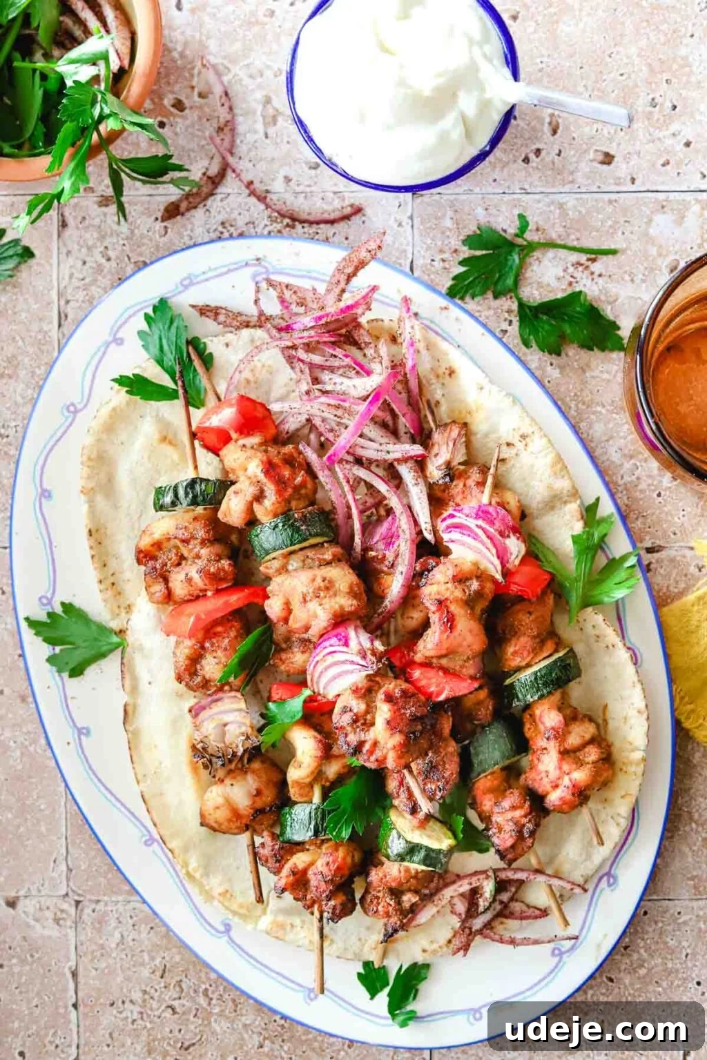 Effortless 15-Minute Air Fryer Chicken Skewers 2 Flavorful air fryer chicken kabobs on a warm pita with creamy sauce, ready to be enjoyed, on a blue-rimmed plate alongside an orange glass and a small bowl of white sauce garnished with fresh parsley.