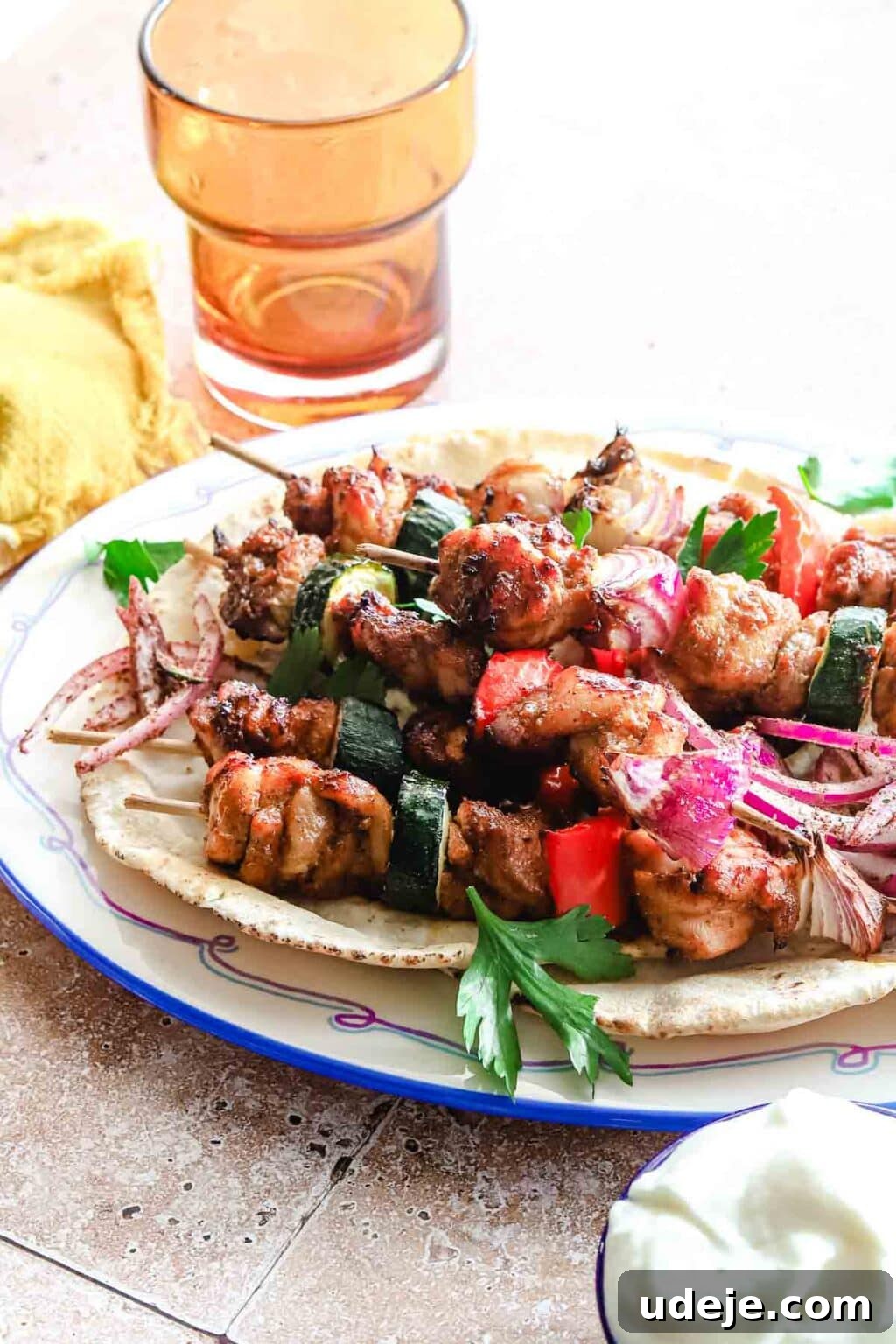 Effortless 15-Minute Air Fryer Chicken Skewers 16 Perfectly cooked air fryer chicken kabobs served on a soft pita, presented on a blue-rimmed plate alongside an orange glass and a yellow tea towel, with a hint of creamy white sauce, inviting a delicious meal.