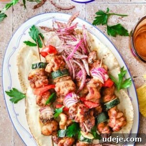 Effortless 15-Minute Air Fryer Chicken Skewers 17 Skewered air fryer chicken kabobs on a pita on a plate with a blue border with an orange glass and a white sauce in a small bowl with a spoon with parsley in the corner