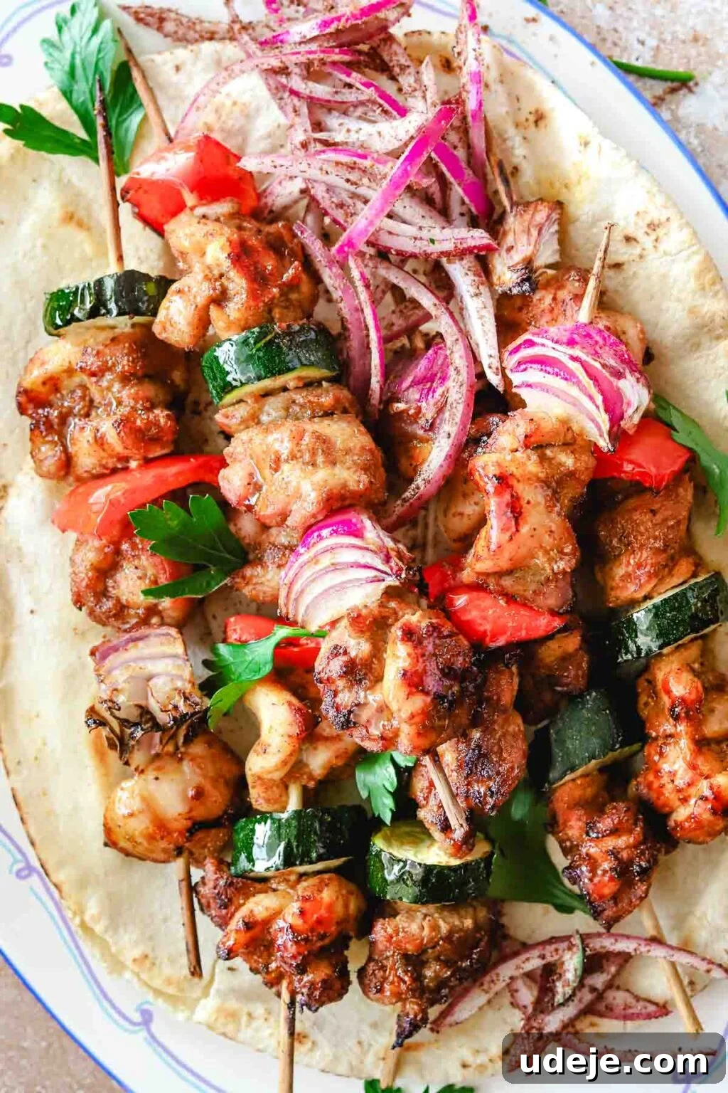 Effortless 15-Minute Air Fryer Chicken Skewers 4 Beautifully cooked air fryer chicken kabobs, glistening and perfectly charred, resting on a soft pita bread on a blue-rimmed plate set against a rustic stone-tiled background.