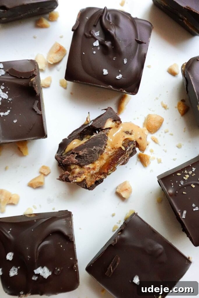 Guilt Free Four Ingredient Snickers Inspired Bites 2 Delicious Healthy Snickers Bites arranged in an ice cube mold, showcasing the layers of dates, peanut butter, peanuts, and chocolate coating.