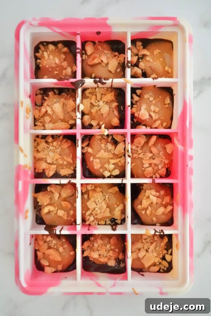 Guilt Free Four Ingredient Snickers Inspired Bites 5 A third image in the series, showing the chocolate coating being poured over the layered Snickers bites in the mold.