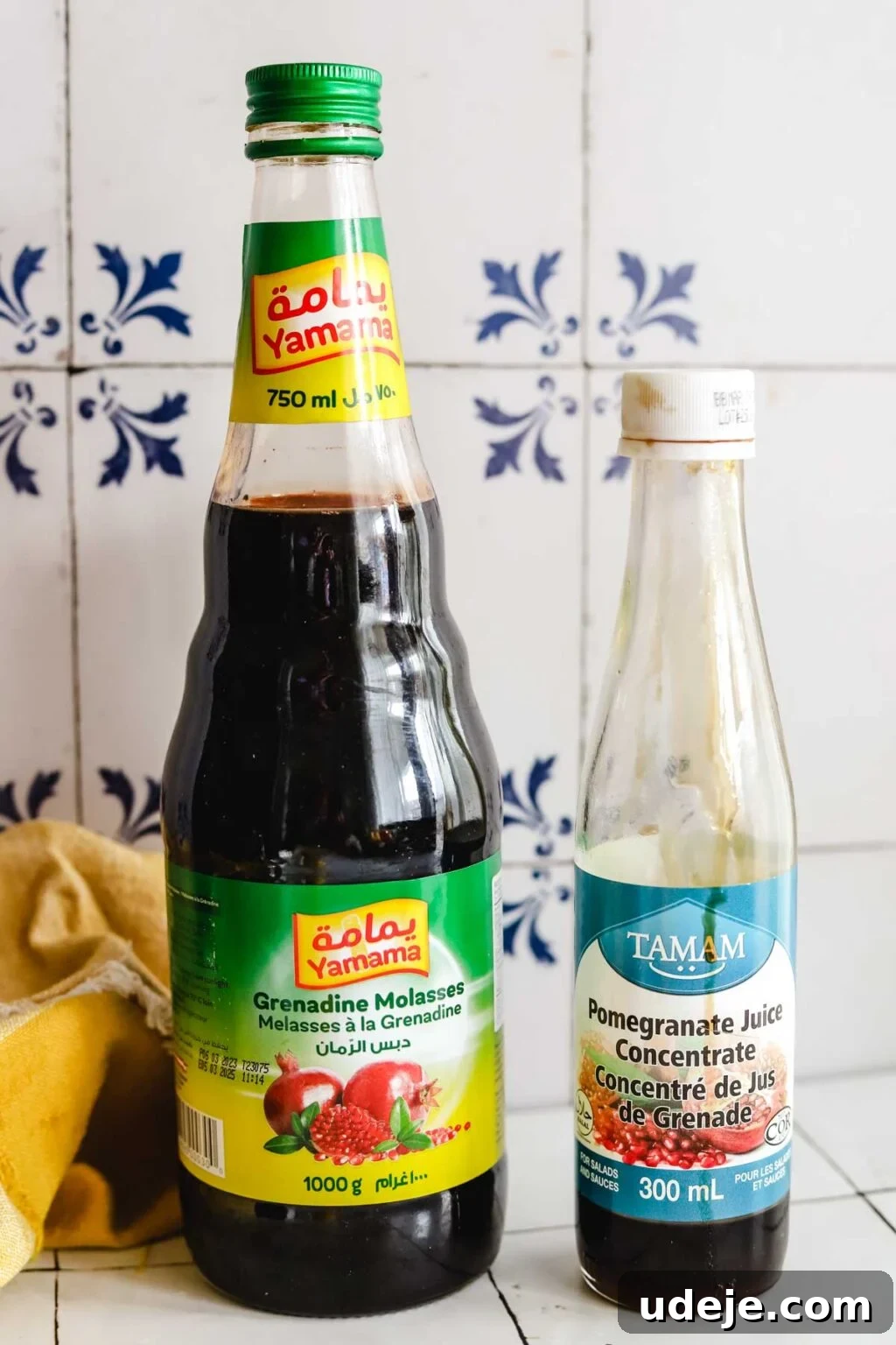 Effortless Arabic Salad 3 Two distinct bottles of pomegranate molasses stand side by side, showcasing their rich, dark hue. A soft yellow kitchen towel provides a warm background, hinting at culinary preparations.