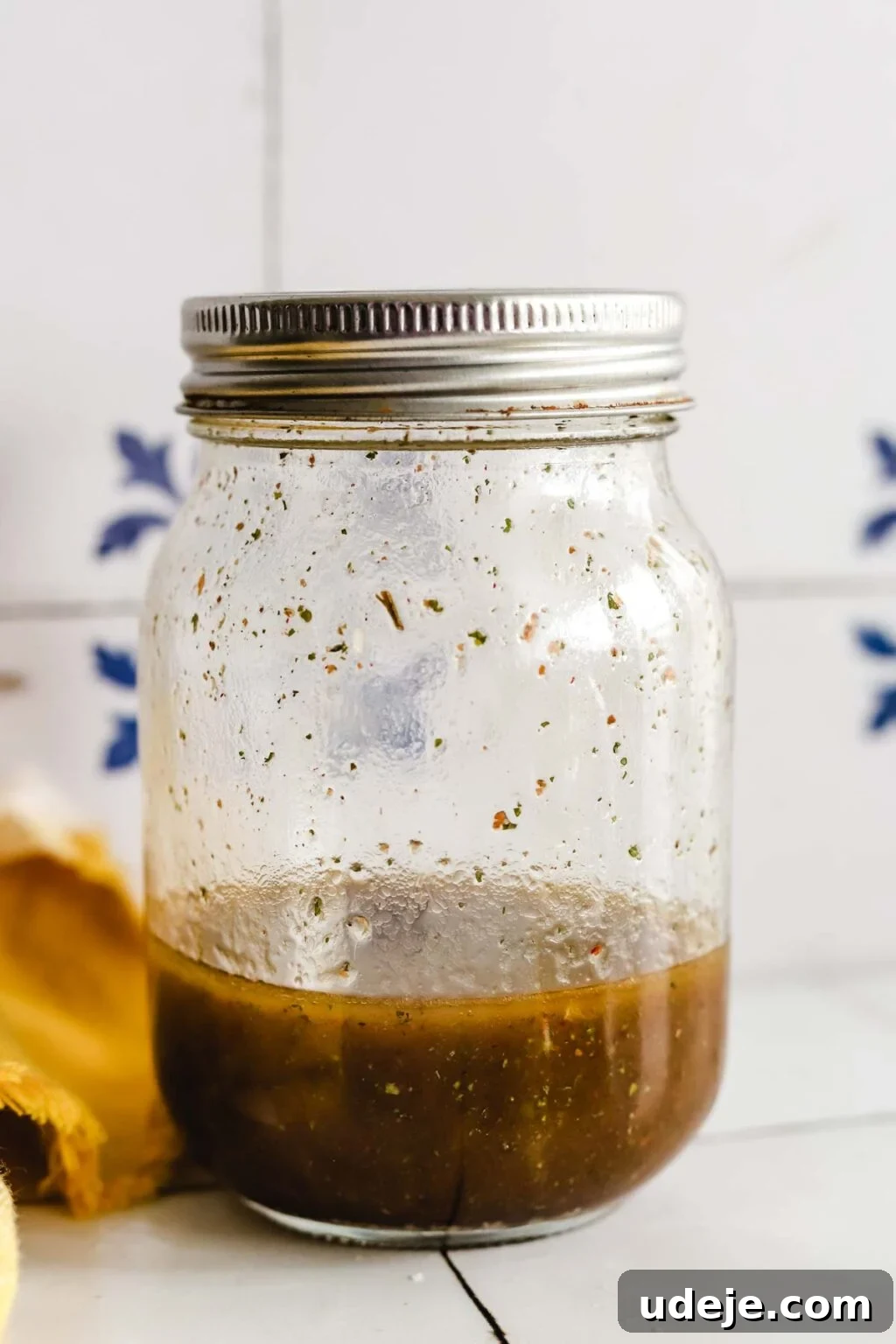 Effortless Arabic Salad 5 A covered mason jar, filled about a quarter of the way with a rich, dark brown salad dressing, rests on a surface next to a yellow kitchen towel.
