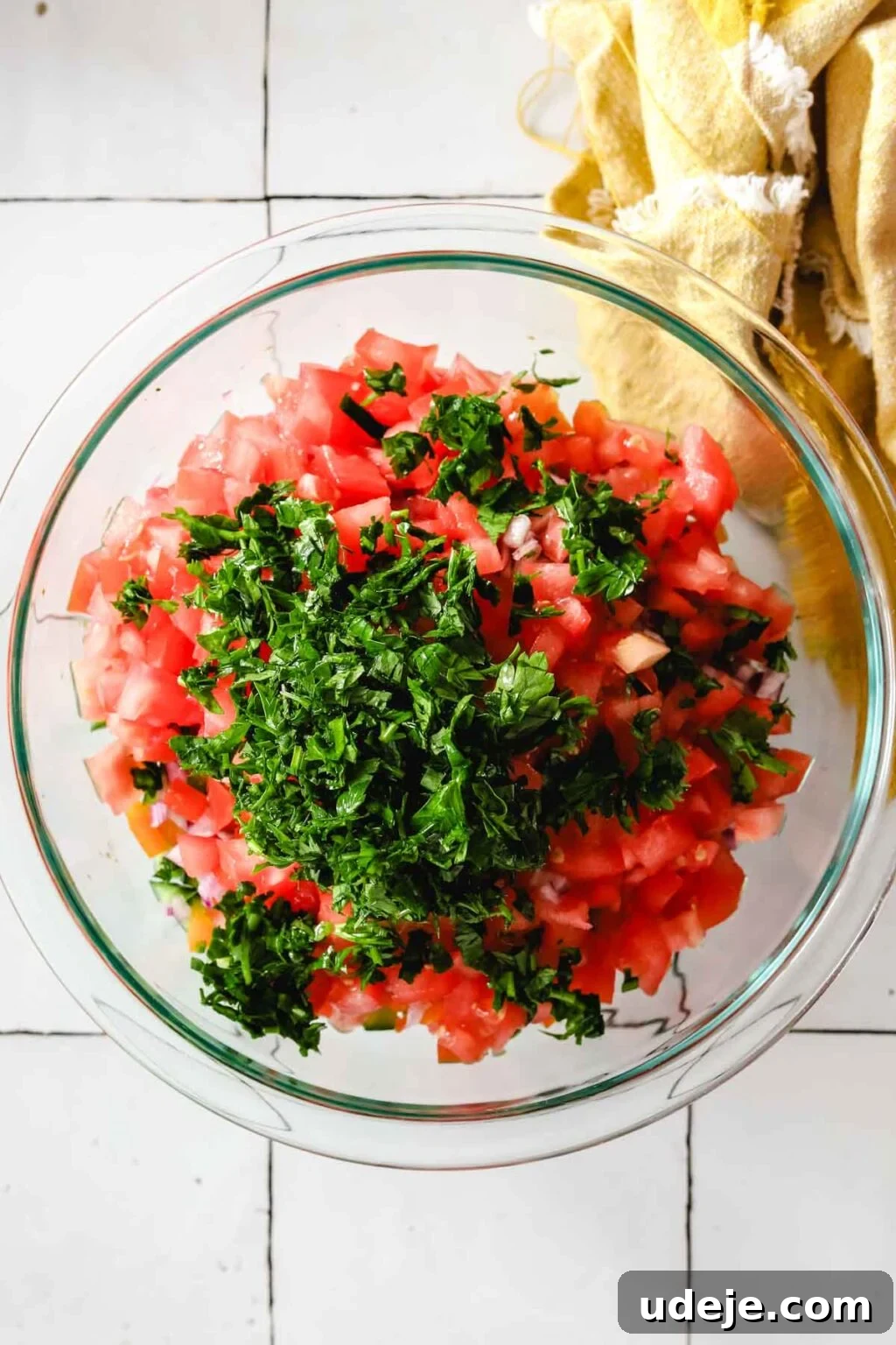 Effortless Arabic Salad 10 A medium glass bowl contains a fresh blend of chopped tomato and vibrant parsley, positioned with a yellow kitchen towel in the top right corner.