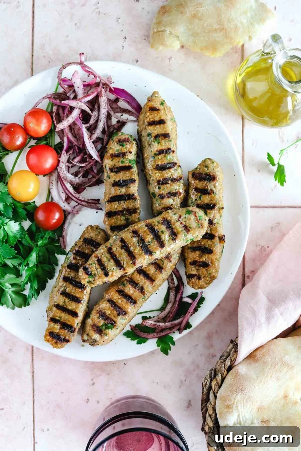 Speedy Chicken Kofta: Grill or Skillet in 20 Minutes 2 Grilled chicken kofta with prominent grill marks, elegantly arranged on a white plate alongside vibrant sliced red onions, juicy cherry tomatoes, and fresh parsley for garnish.