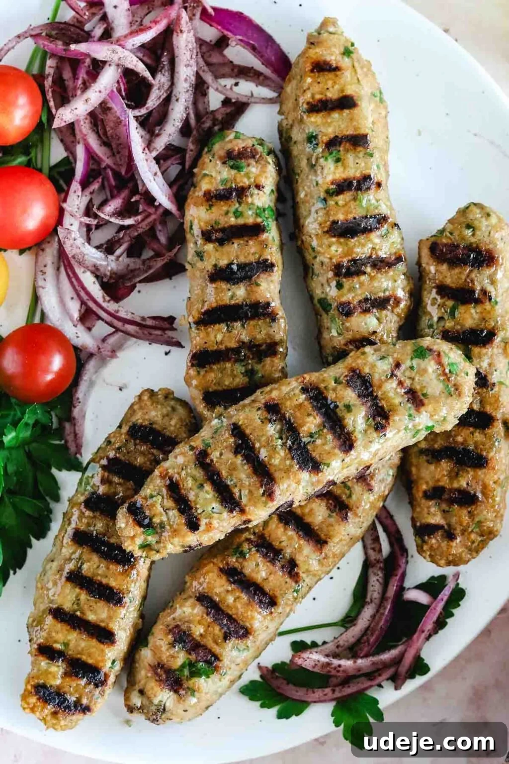 Speedy Chicken Kofta: Grill or Skillet in 20 Minutes 11 Delicious grilled chicken kofta with characteristic grill marks, beautifully plated on a white dish, accompanied by fresh sliced red onions, sweet cherry tomatoes, and a sprinkle of vibrant parsley.