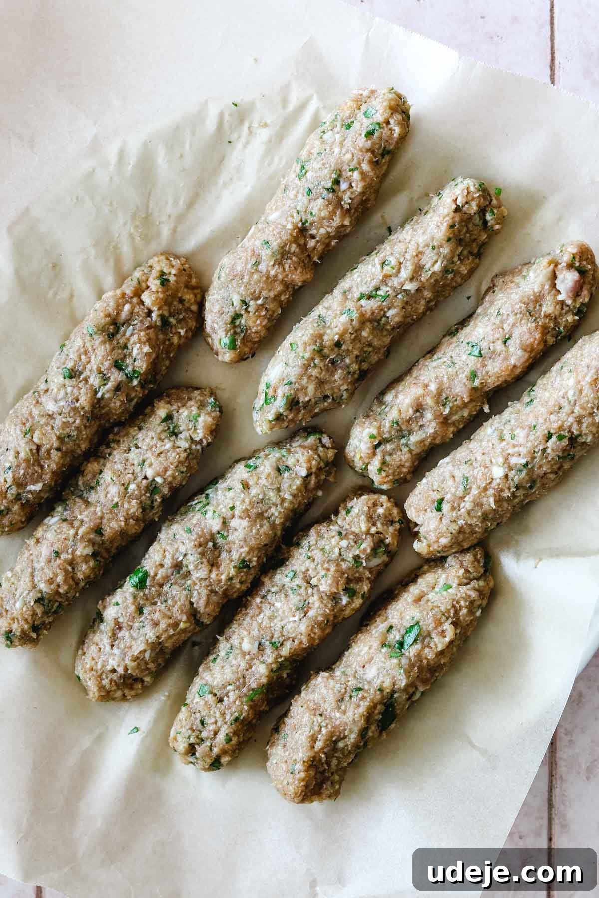 Speedy Chicken Kofta: Grill or Skillet in 20 Minutes 8 Perfectly shaped uncooked chicken kofta logs, neatly arranged on a plate lined with parchment paper, ready for cooking.