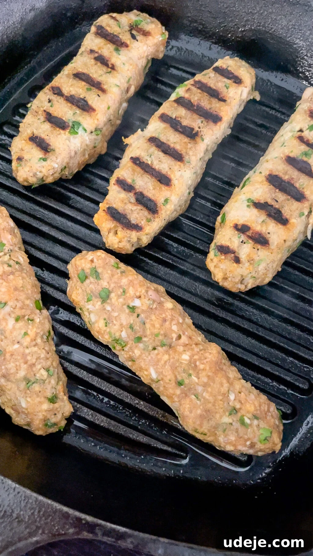 Speedy Chicken Kofta: Grill or Skillet in 20 Minutes 10 Chicken koftas actively grilling on a cast iron pan, showing distinct black grill marks on several pieces, indicating perfect searing.