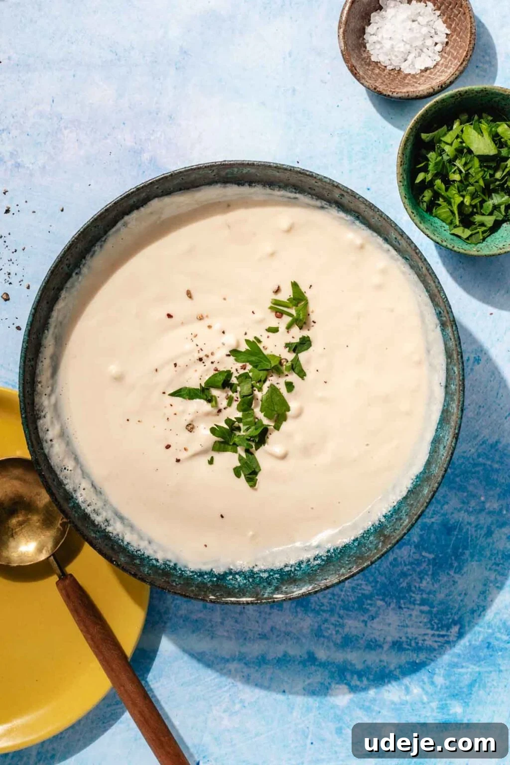 Simple & Creamy 3-Ingredient Tahini Sauce 2 A vibrant, creamy tahini sauce in a beautiful blue stoneware bowl, artfully garnished with a sprinkle of coarse ground black pepper and freshly chopped parsley, inviting a delightful culinary experience.