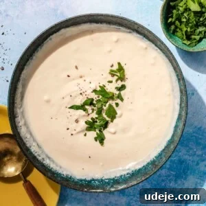 A beautifully presented tahini sauce in a blue stoneware bowl, garnished with freshly ground black pepper and finely chopped parsley, ready to be enjoyed.
