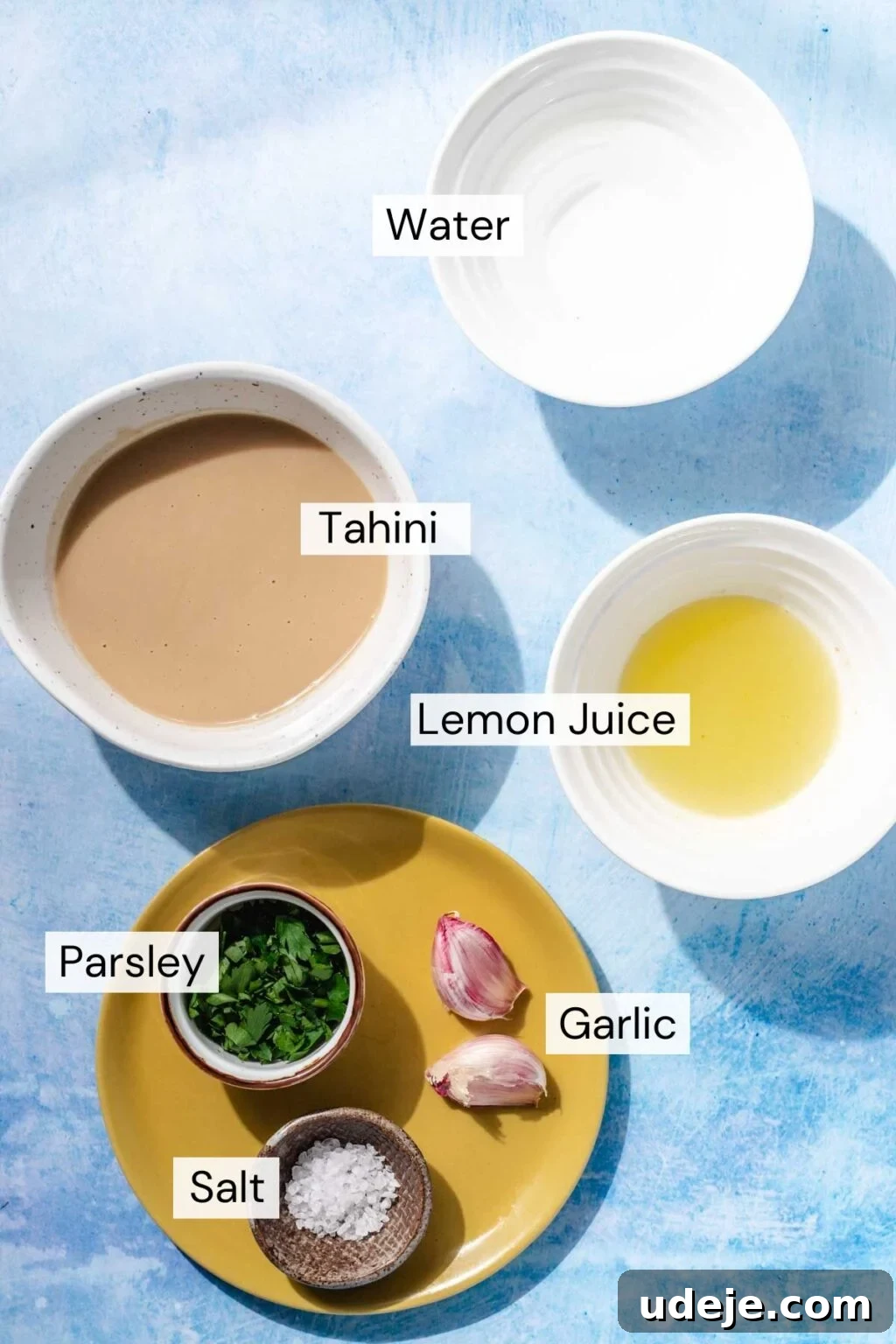 Simple & Creamy 3-Ingredient Tahini Sauce 3 The essential ingredients for crafting perfect tarator sauce: creamy tahini, refreshing water, zesty lemon juice, potent garlic, fine salt, and vibrant fresh parsley, all ready for mixing.