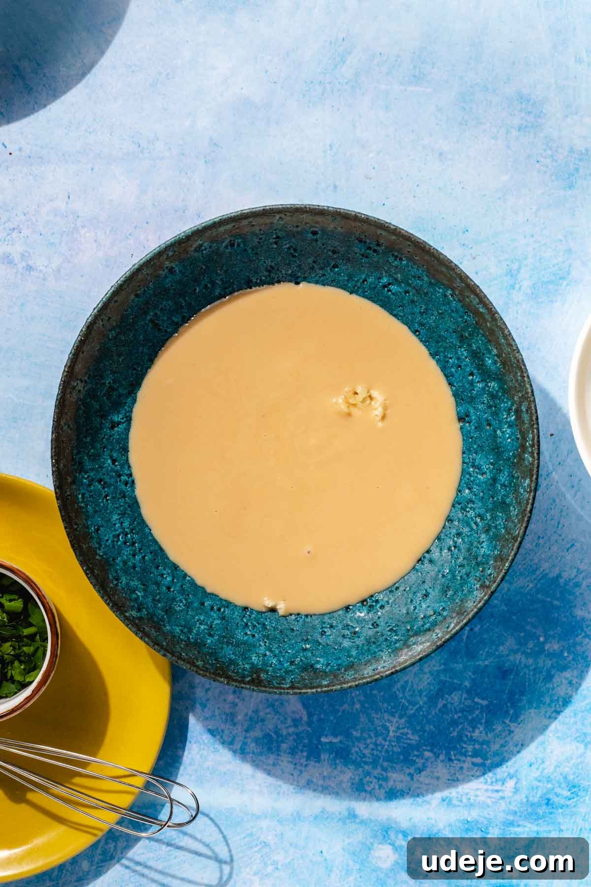 Simple & Creamy 3-Ingredient Tahini Sauce 5 A close-up view of crushed garlic combined with creamy tahini in a blue stone bowl, highlighting the initial mixture before liquids are added.