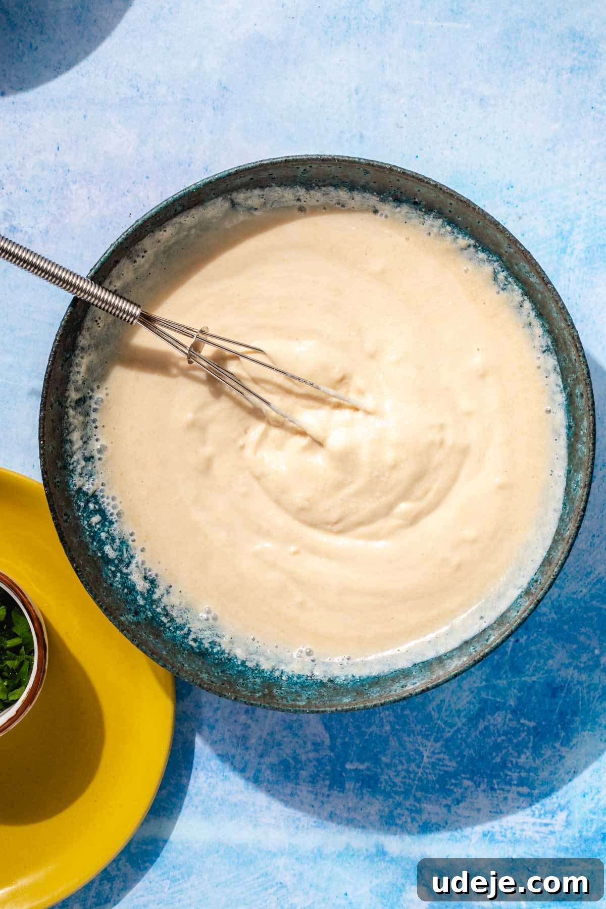 Simple & Creamy 3-Ingredient Tahini Sauce 7 The tahini sauce, now whisked to a smooth, creamy, and light consistency, presented in a blue stone bowl with a small whisk, showcasing the successful emulsification of ingredients.