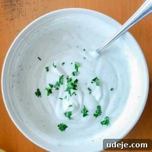 white bowl with shawarma sauce and herbs on top and a spoon in it on an orange background with a half lemon at the side