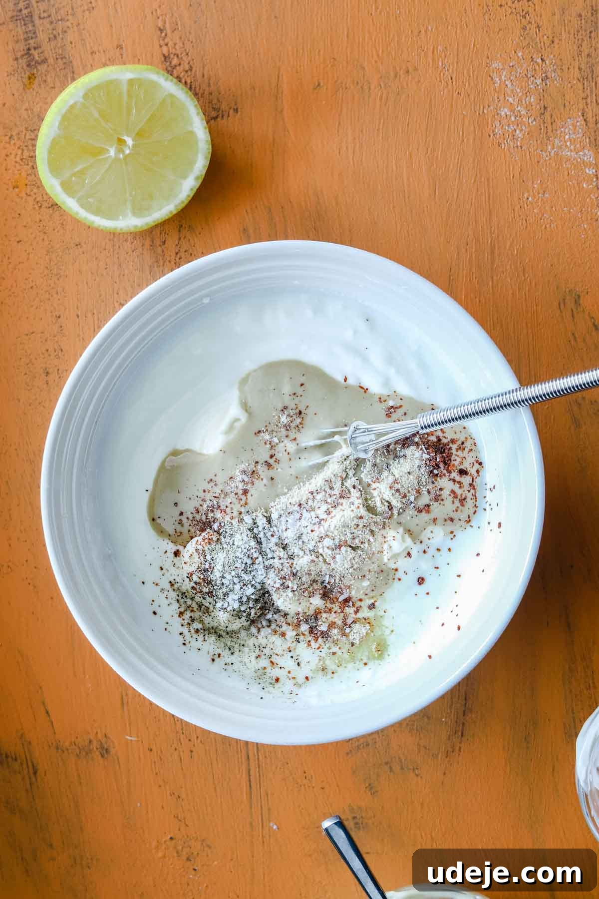 Creamy 5-Minute Shawarma Sauce 5 White bowl with yogurt, mayonnaise, tahini, lemon juice and spices with a whisk on an orange backdrop with a half lemon on the side