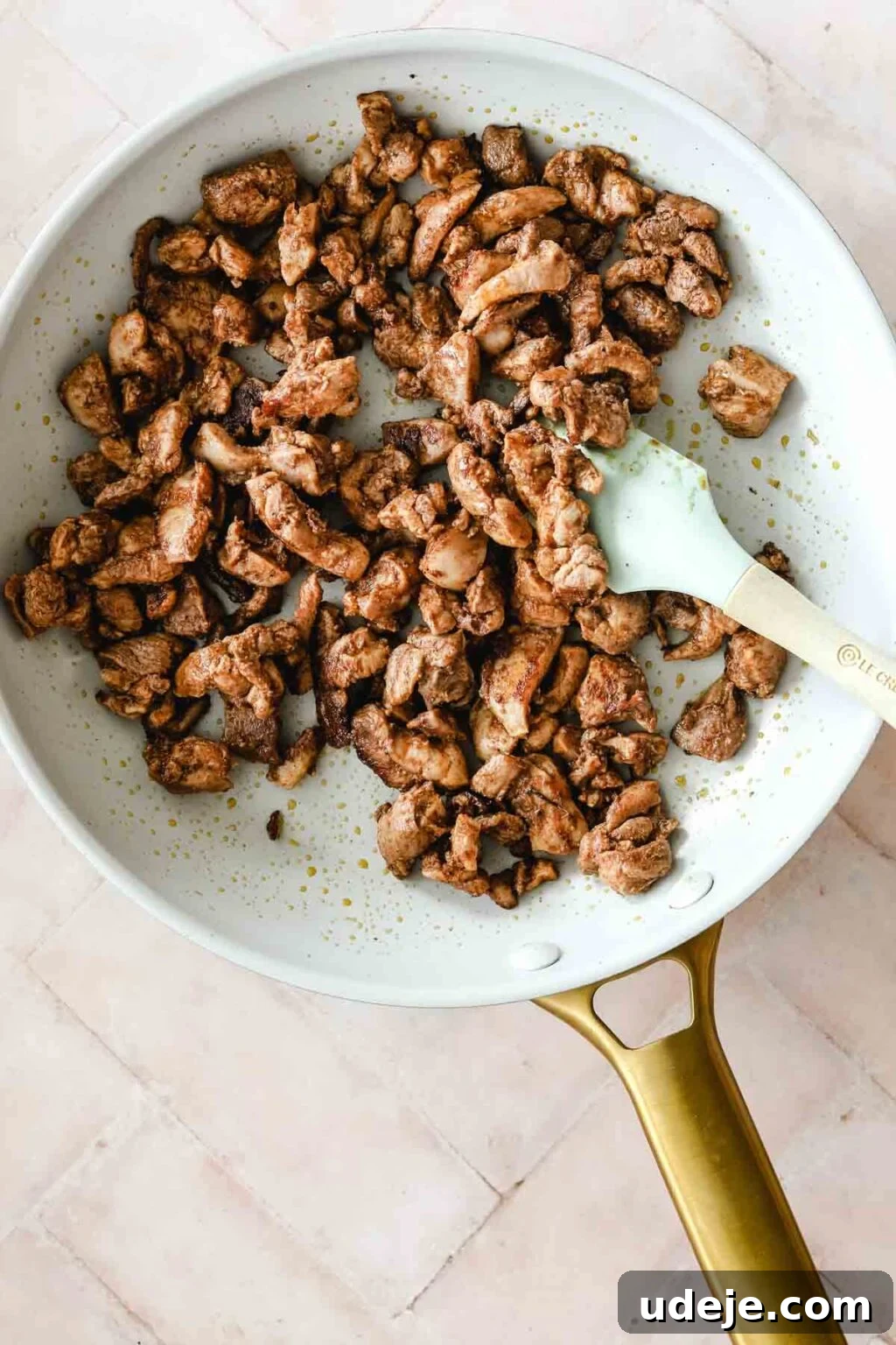 Cooked chicken shawarma sizzling in a medium skillet with a gold handle, a teal spatula resting on the side, ready to be added to the fresh salad ingredients.