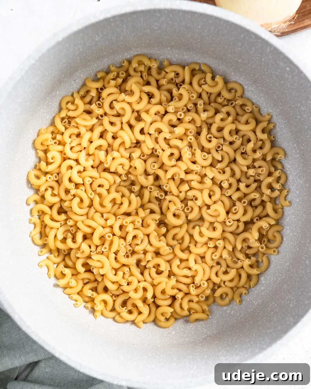 Egypt's Koshari: A Hearty Blend of Rice, Lentils and Pasta 14 raw macaroni in a light coloured pot with a green towel at the side and an onion at the top