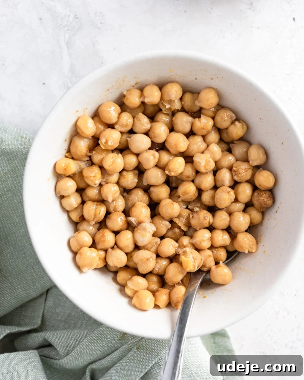 Egypt's Koshari: A Hearty Blend of Rice, Lentils and Pasta 16 a white bowl of spiced chickpeas with a spoon in it with a green towel at the side on a light grey marble background