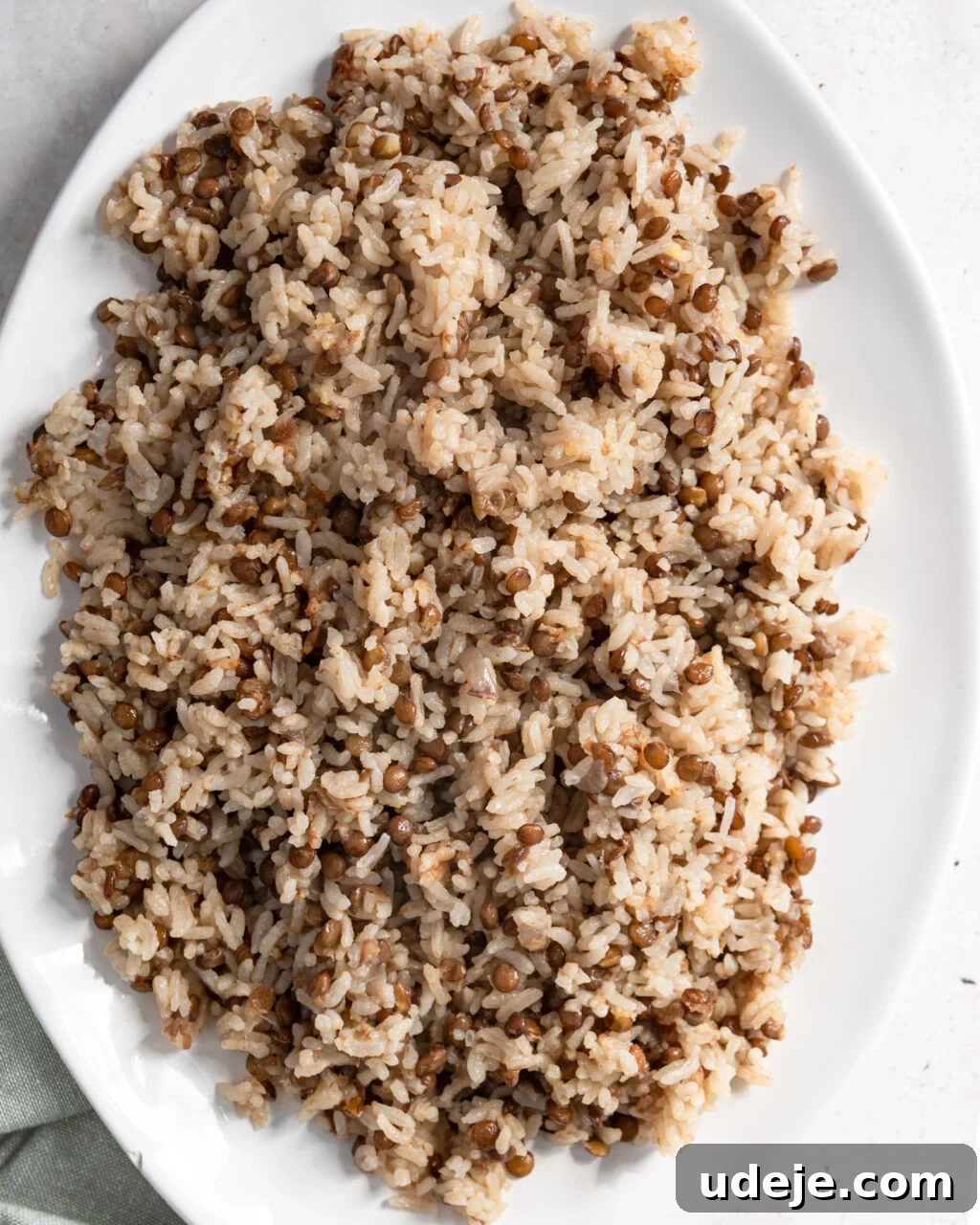 Egypt's Koshari: A Hearty Blend of Rice, Lentils and Pasta 20 Cooked rice and lentils on a white platter with a green towel at the side on a light coloured background