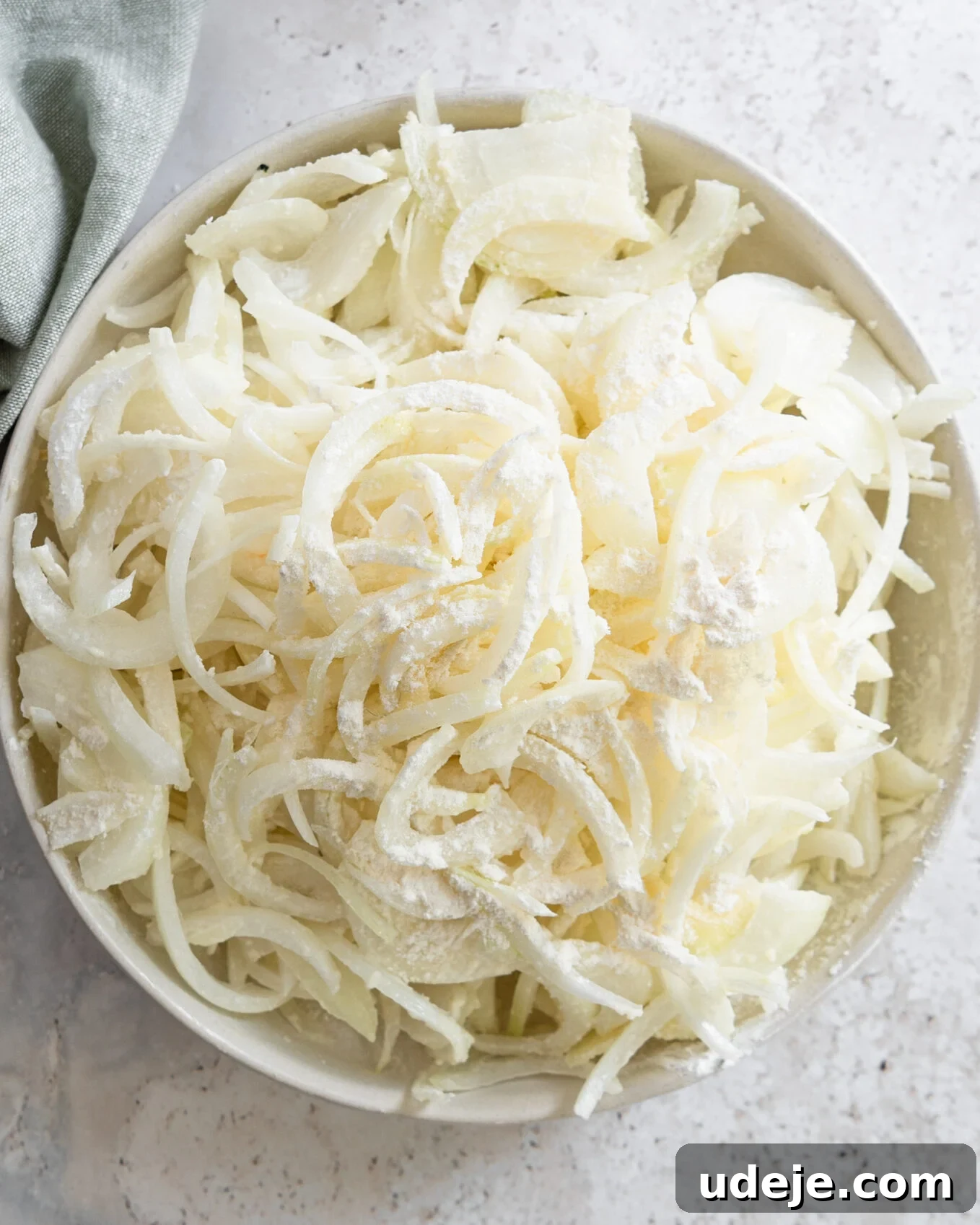 Egypt's Koshari: A Hearty Blend of Rice, Lentils and Pasta 5 sliced white onions with flour in a white bowl with a green towel on a light grey marble background