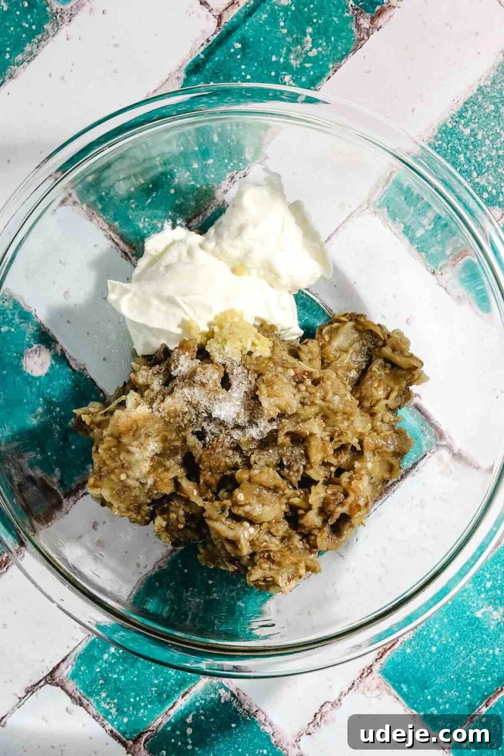 Ali Nazik Smoky Eggplant and Lamb Stew 12 Chopped eggplant fles with seasonings and strained yogurt in a glass bowl on a teal and white brick background