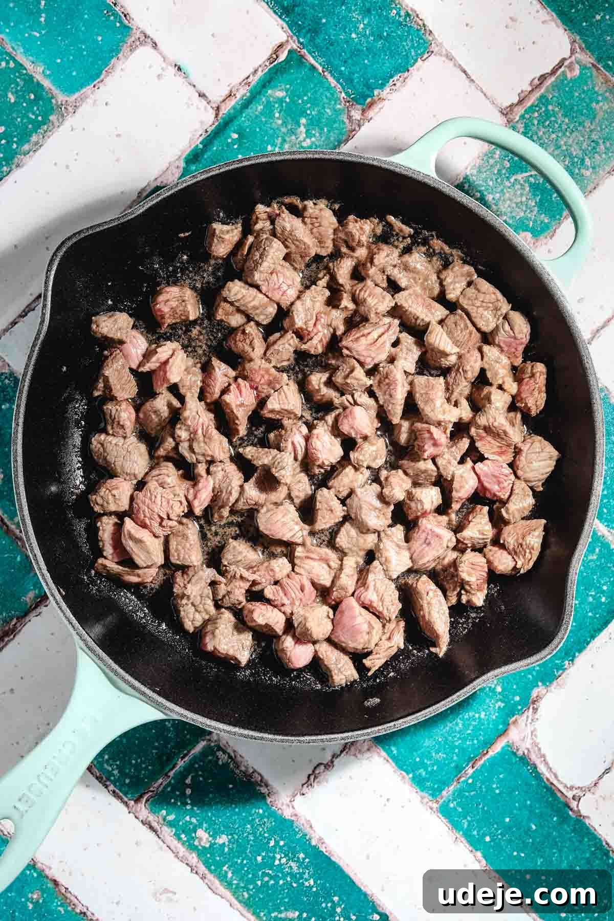 Ali Nazik Smoky Eggplant and Lamb Stew 14 Veal or lamb cubes being brownedin a light blue cast iron pan on a teal and white brick background