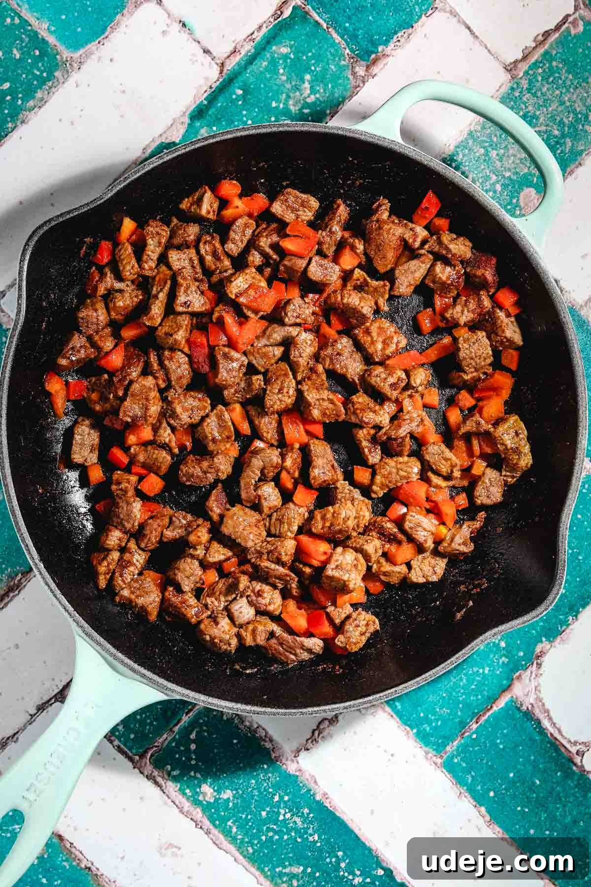 Ali Nazik Smoky Eggplant and Lamb Stew 15 Browned veal or lamb cubes with chopped red pepper in a light blue cast iron pan on a teal and white brick background