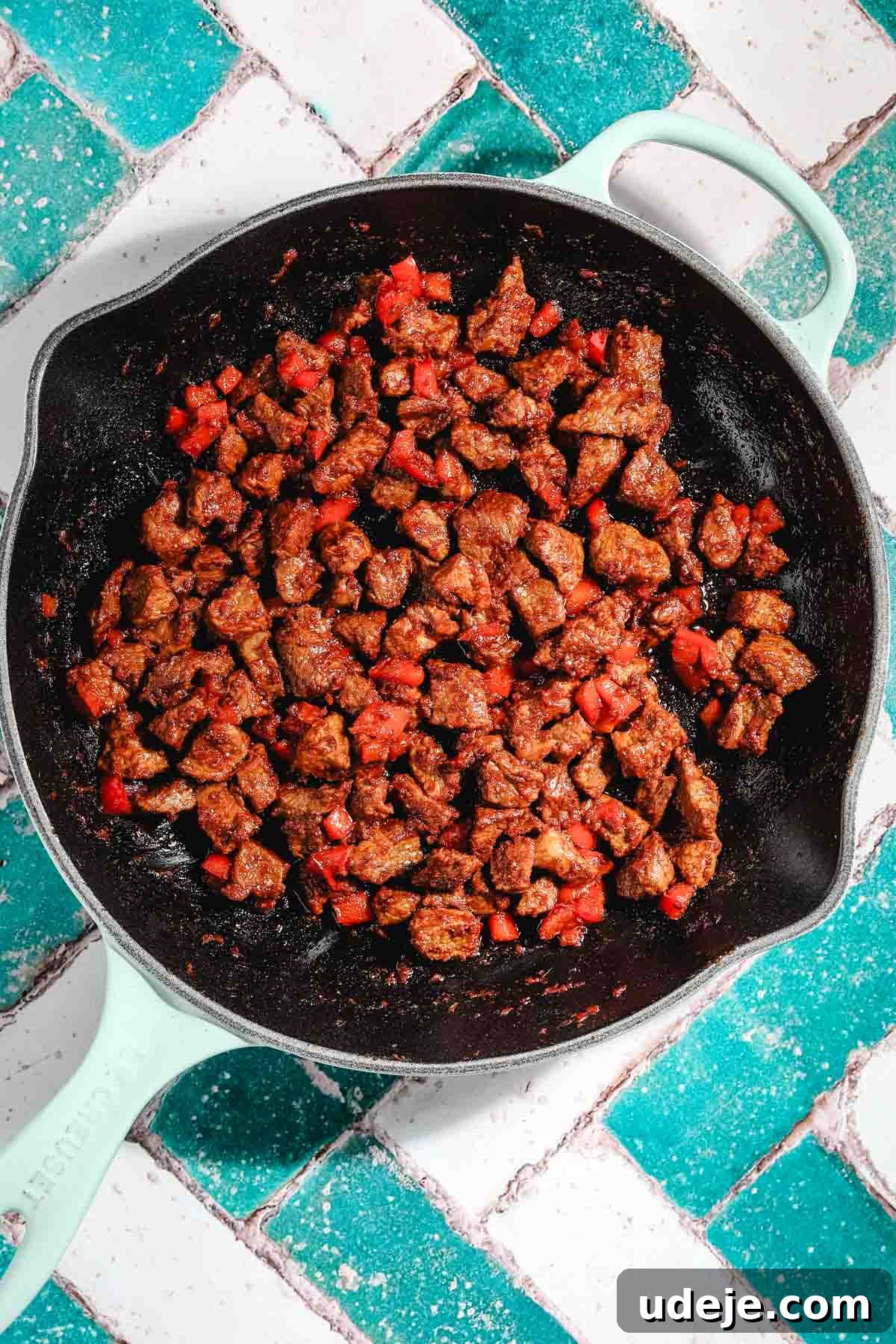 Ali Nazik Smoky Eggplant and Lamb Stew 16 Cooked veal or lamb cubes with cooked red peppers in a light blue cast iron pan on a teal and white brick background
