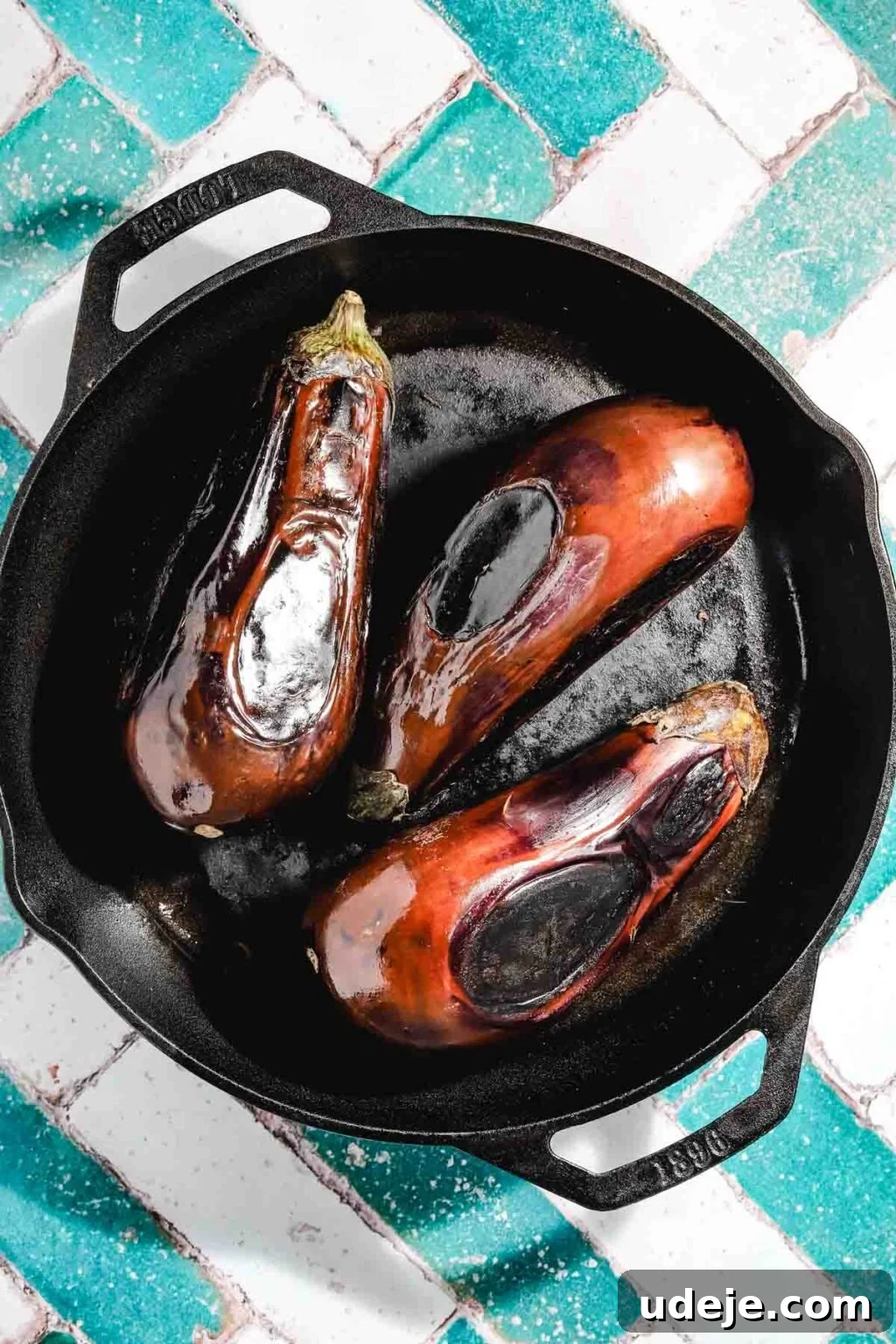 Ali Nazik Smoky Eggplant and Lamb Stew 5 Three eggplants that have been charred in a cast iron pan on a teal and white brick background