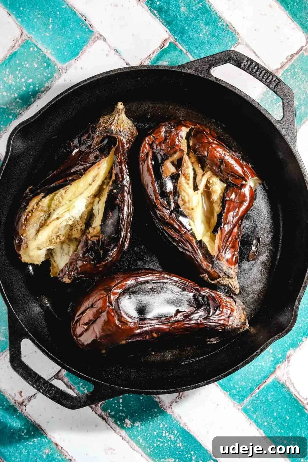 Ali Nazik Smoky Eggplant and Lamb Stew 6 Three charred eggplants that have been split open on a cast iron pan on a teal and white brick background