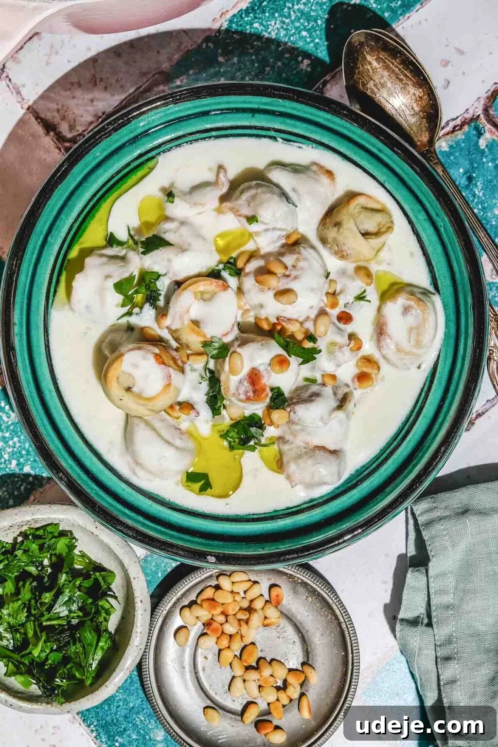 Mastering Homemade Shish Barak: Authentic Yogurt Dumplings 2 Shish Barak, meat-filled dumplings served in a savory yogurt sauce, garnished with toasted pine nuts, chopped parsley, and a drizzle of olive oil, presented in a teal-colored plate.