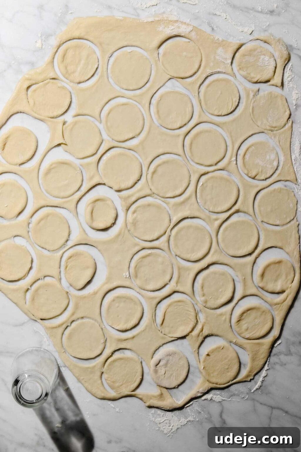 Mastering Homemade Shish Barak: Authentic Yogurt Dumplings 11 Small circular dough cutouts for Shish Barak, arranged on a floured surface with a glass cup used as a cutter, indicating the precise shaping process.