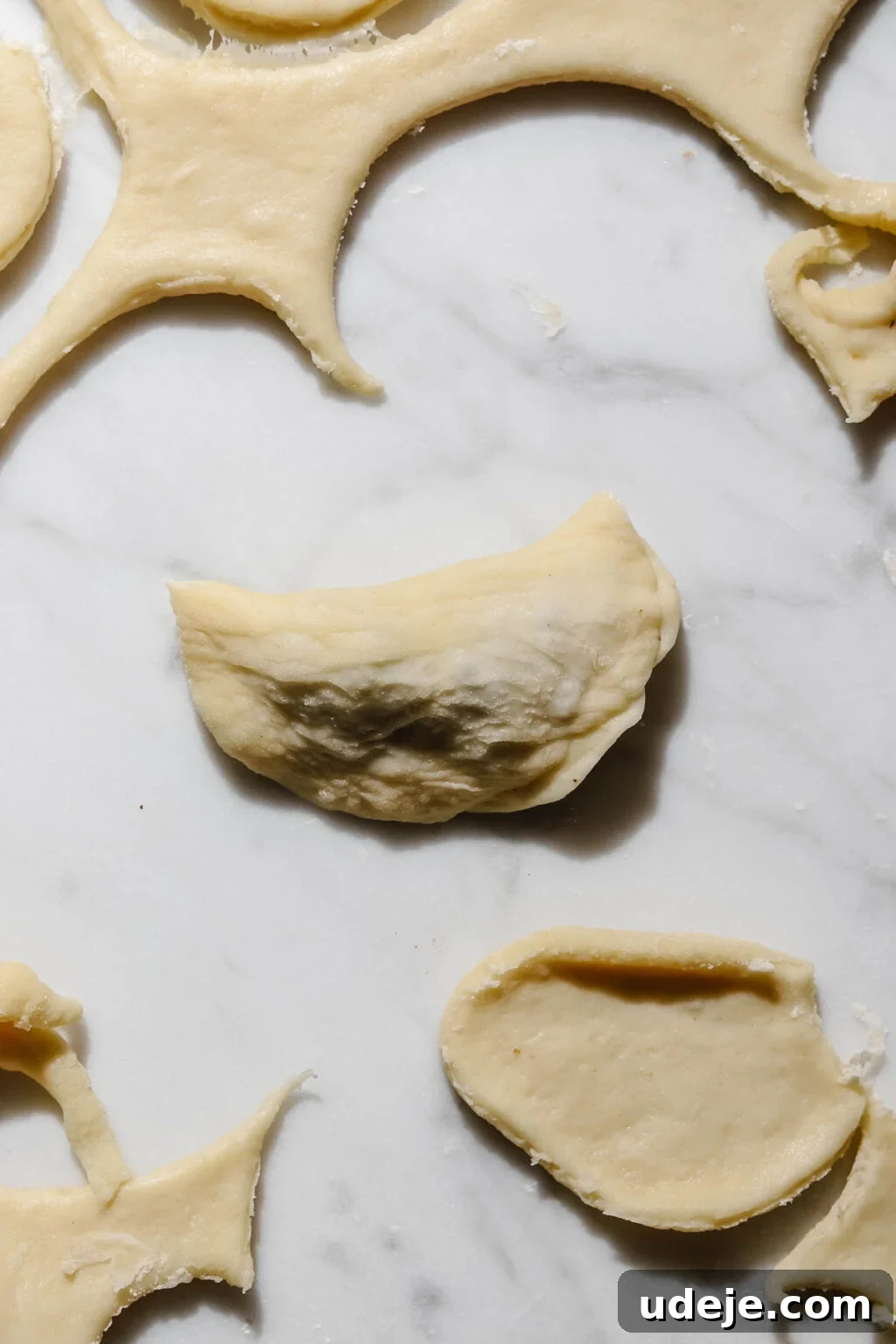 Mastering Homemade Shish Barak: Authentic Yogurt Dumplings 14 A small half-circle dough filled with Shish Barak meat filling, with surrounding dough scraps and cutouts, demonstrating the initial folding step on a light marble background.