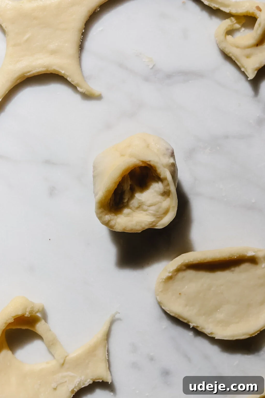 Mastering Homemade Shish Barak: Authentic Yogurt Dumplings 15 A Shish Barak dumpling, folded into a half-circle and pinched at the ends to form a tortellini shape, showcasing the intricate final shaping step amidst dough scraps and cutouts on a light marble background.