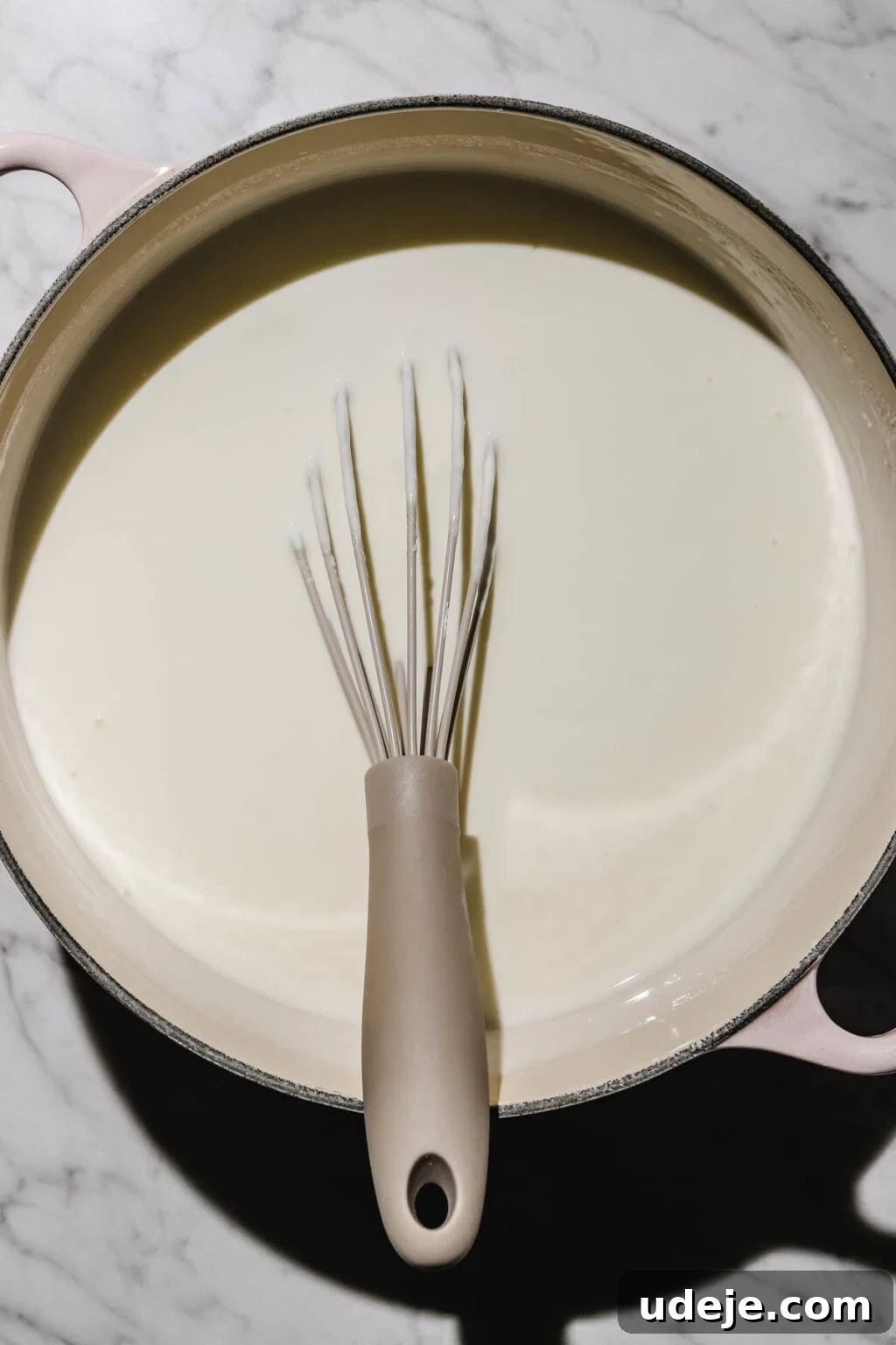 Mastering Homemade Shish Barak: Authentic Yogurt Dumplings 18 Yogurt mixture being whisked in a pink-handled pot on a light marbled background, ensuring a smooth consistency before heating.