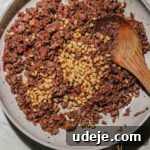 cooked ground beef shish barak filling with toasted pine nuts on top in a light grey skillet with a wooden spoon on a light marble background