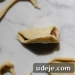 small circle of dough folded over with cut out dough around it with meat filling in the middle of the folded over circle on a light marble background
