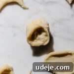 half circle folded and pinched at the ends with shish barak meat filling inside with scraps of dough and circle cutouts of dough around it on a light marble background