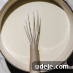 yogurt in a pink handled pot with a whisk in it on a light marbled background