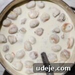 shish barak in yogurt sauce in a pink handled pot with a metal ladle inside on a light marble background