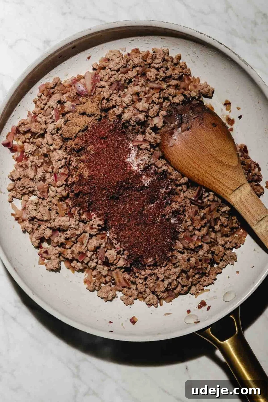 Mastering Homemade Shish Barak: Authentic Yogurt Dumplings 7 Cooked ground beef with onions and Middle Eastern spices in a light grey skillet, stirred with a wooden spoon on a light marble surface.