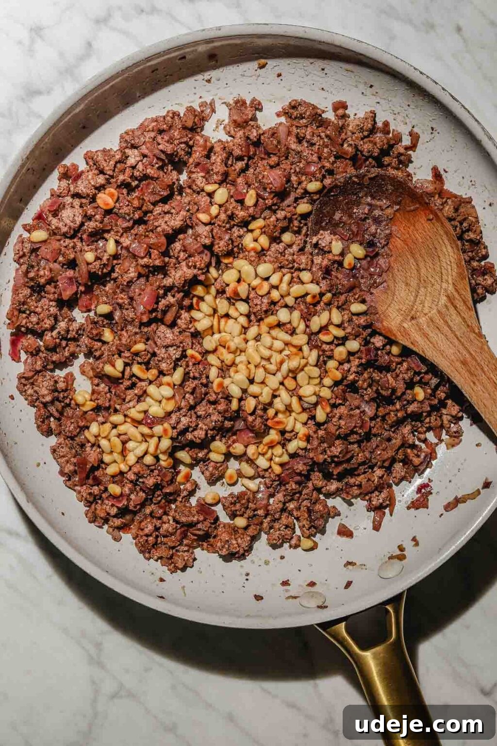 Mastering Homemade Shish Barak: Authentic Yogurt Dumplings 8 The cooked Shish Barak filling, adorned with toasted pine nuts, cooling in a light grey skillet with a wooden spoon on a light marble background.